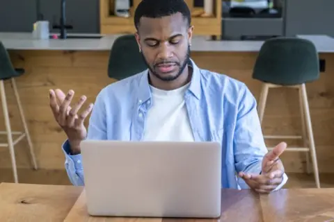 Confused man gesturing at his laptop