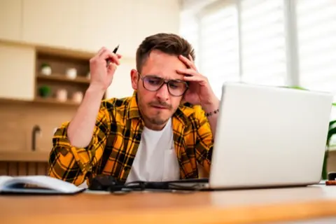 Stressed man in a plaid shirt with a pen in his hand at the laptop