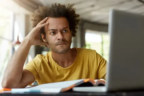 Pensive man resting his head on his hand next to the laptop